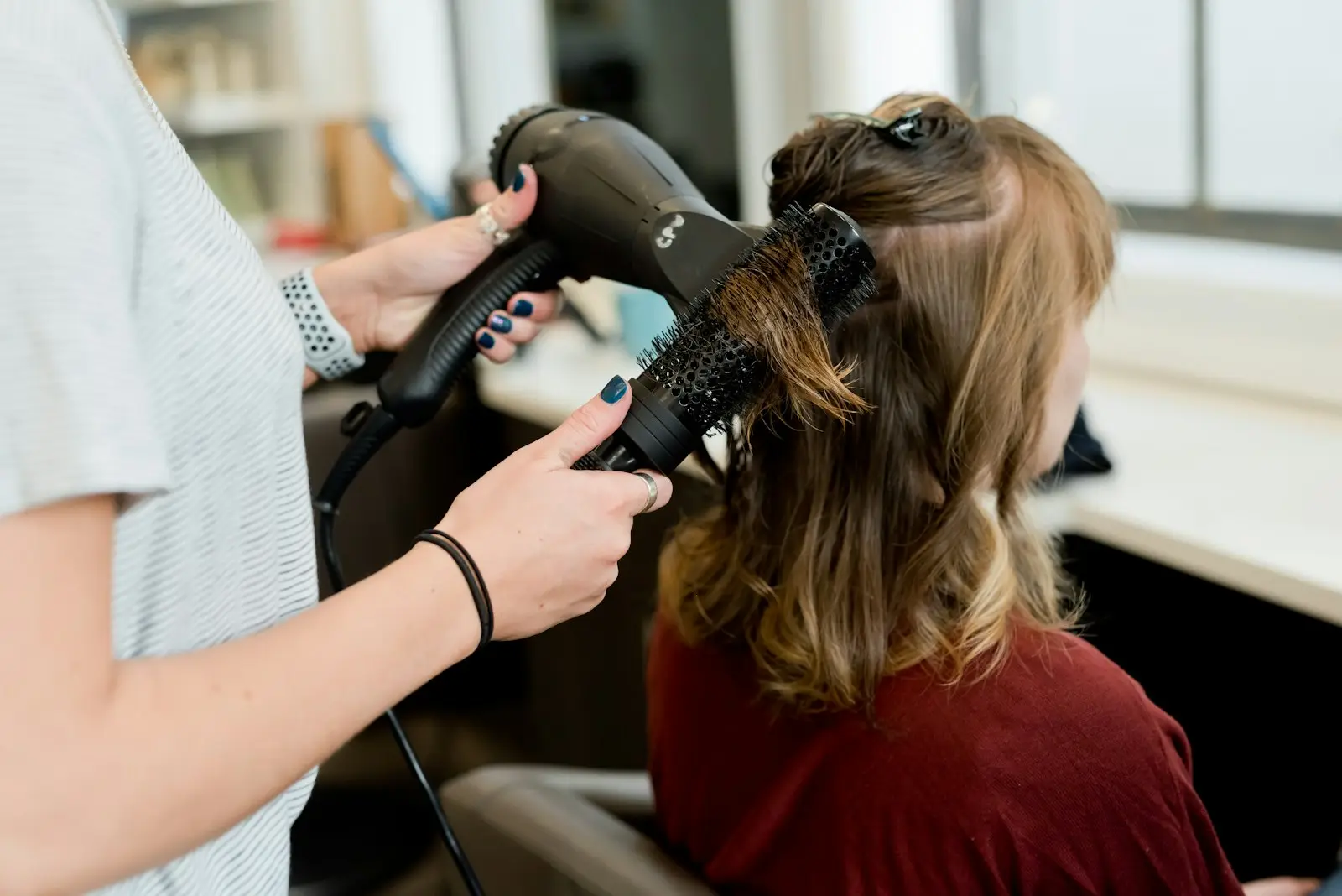 Une coiffeuse fait un brushing avec une brosse ronde et un sèche-cheveux