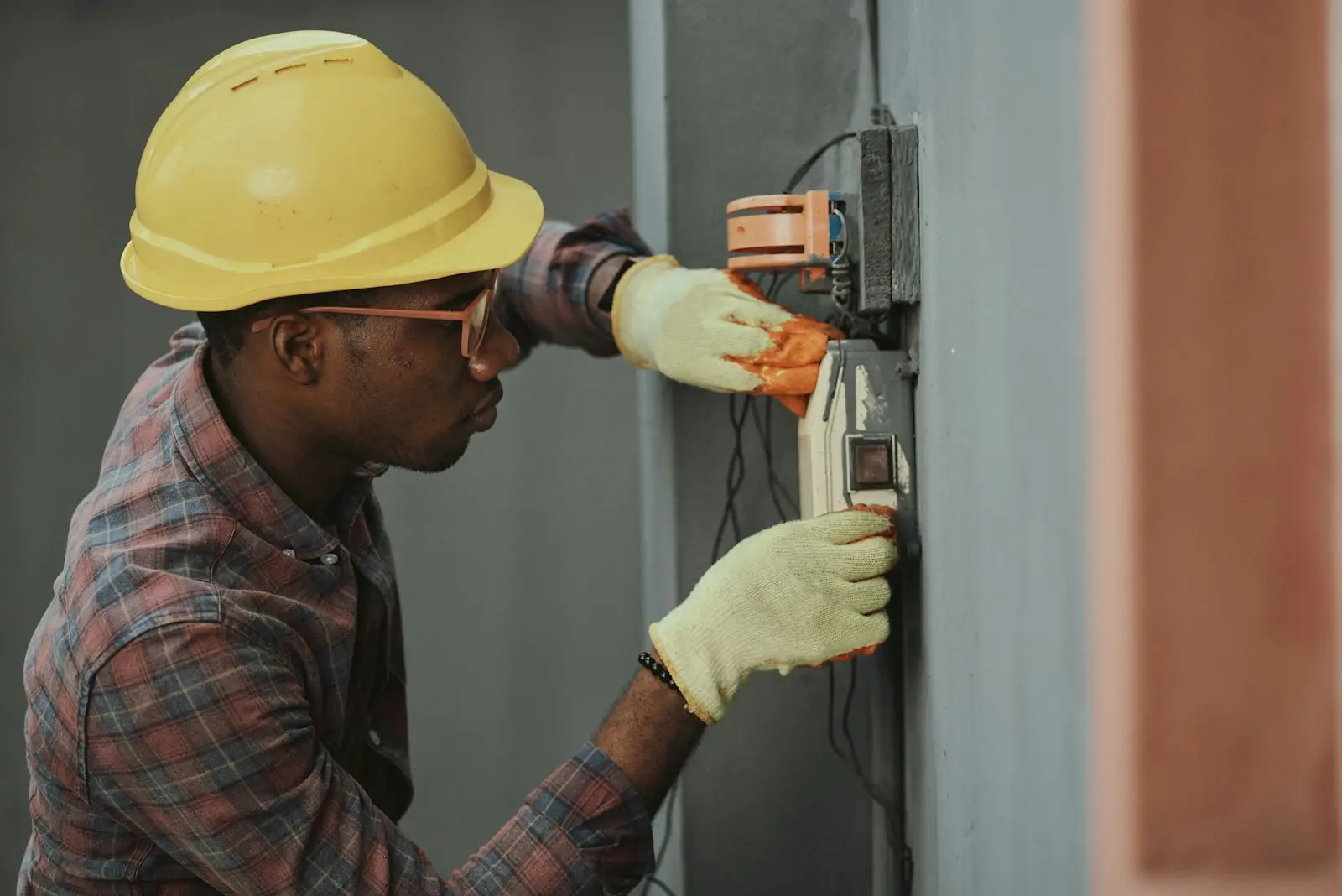 Électricien en casque jaune et gants qui installe un câblage le long d'un mur
