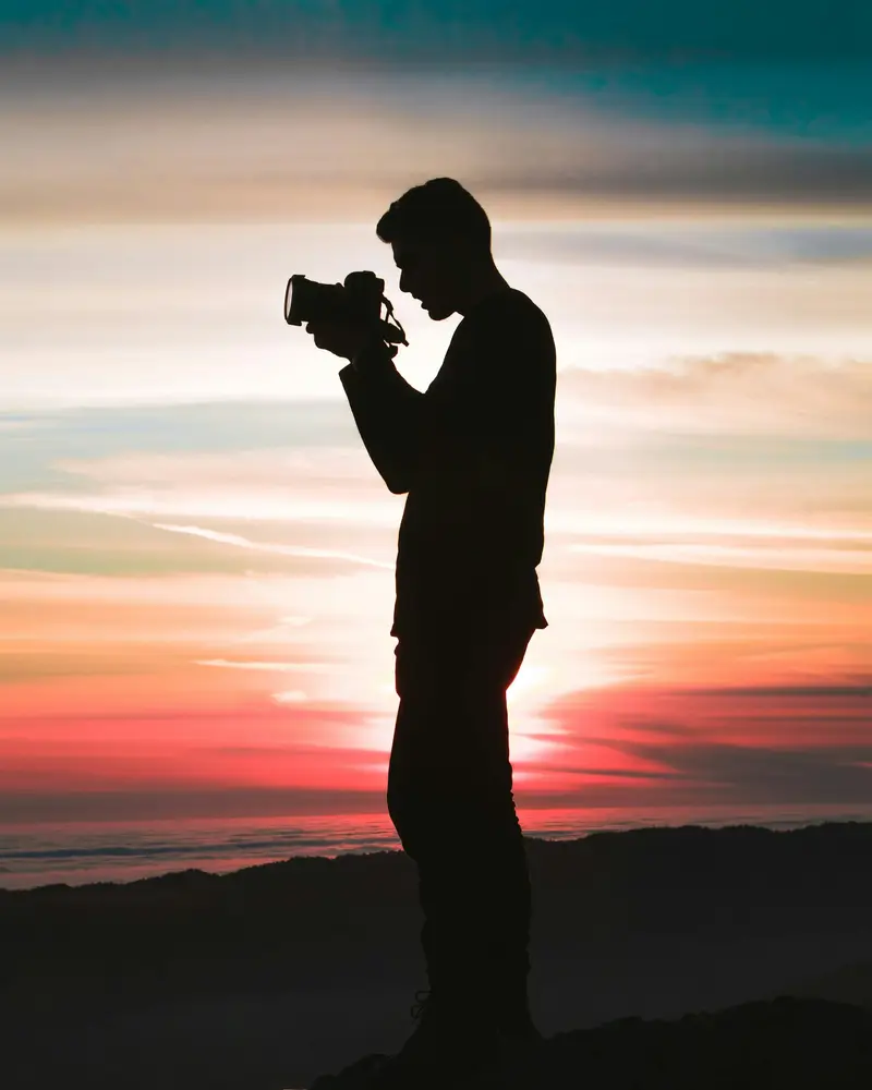 Silhouette d'un homme qui photographie face au coucher de soleil