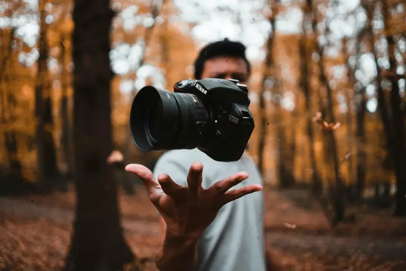 Appareil photo qui semble flotter au-dessus d'une main, dans une forêt d'automne