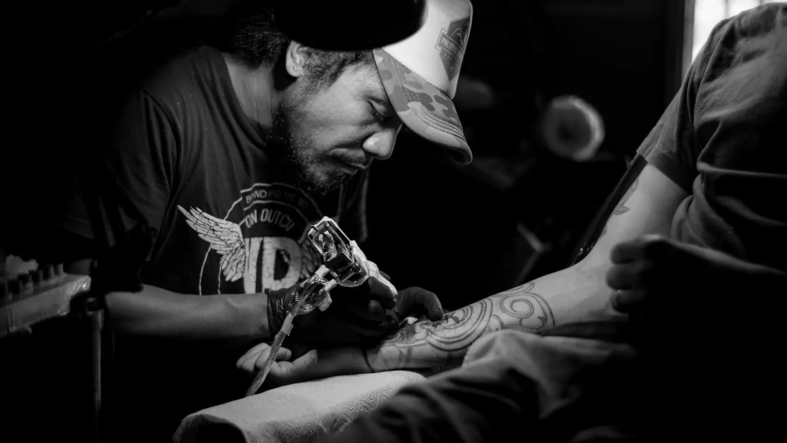 Tatoueur en casquette, concentré sur un bras, photo en noir et blanc